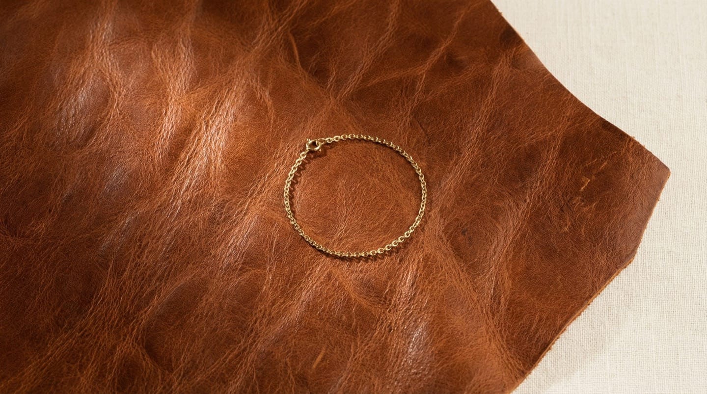 Close-up of genuine full-grain cognac leather texture with natural grain pattern and a gold chain bracelet